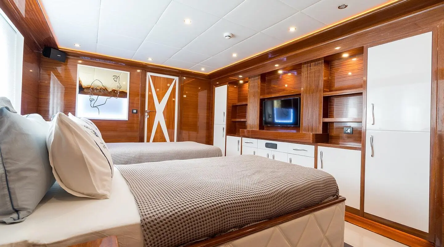Inside a yacht cabin with two large beds, wood paneling, and a TV on the wall