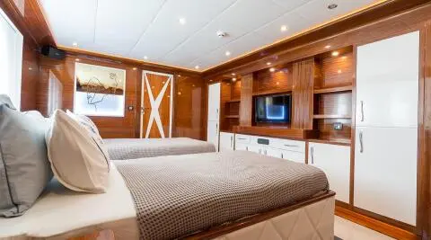 Inside a yacht cabin with two large beds, wood paneling, and a TV on the wall