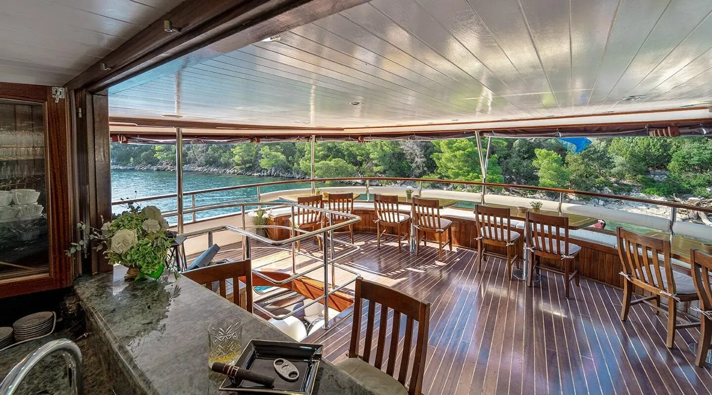 Cesarica yacht interior on deck with wooden chairs and railing at sunset