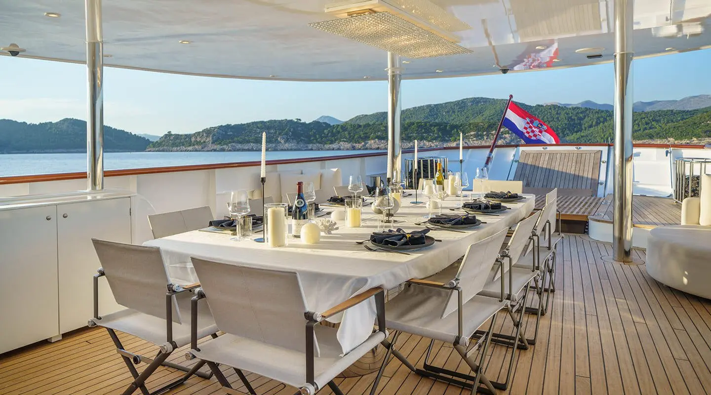 Maia yacht dining area on deck at sunset with table set and chairs