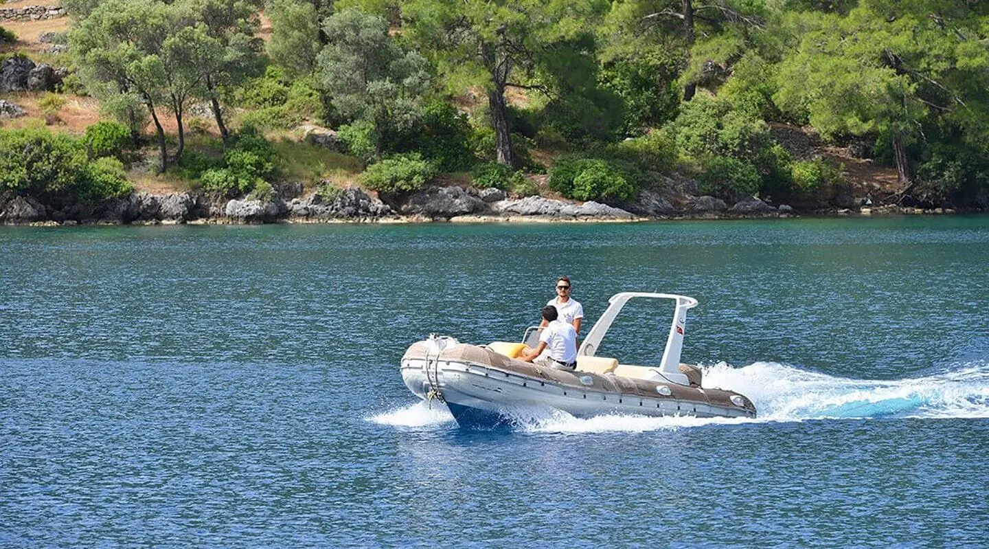Derin Deniz yacht nearby rocky coastline with a small motorboat on calm blue water