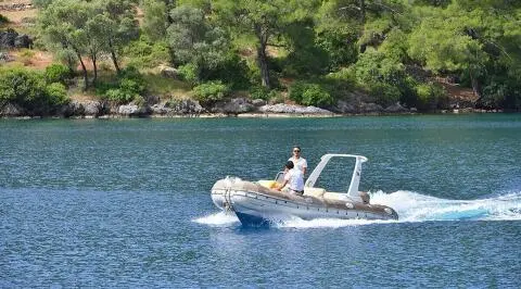Derin Deniz yacht nearby rocky coastline with a small motorboat on calm blue water