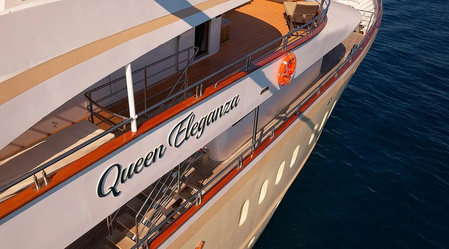 Queen Eleganza yacht anchored with red hull and reflection in calm blue water.