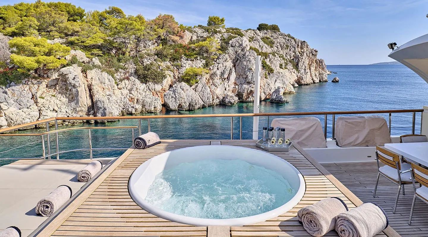 La Pellegrina 1 yacht with a circular hot tub on aft deck and rocky coastline in background