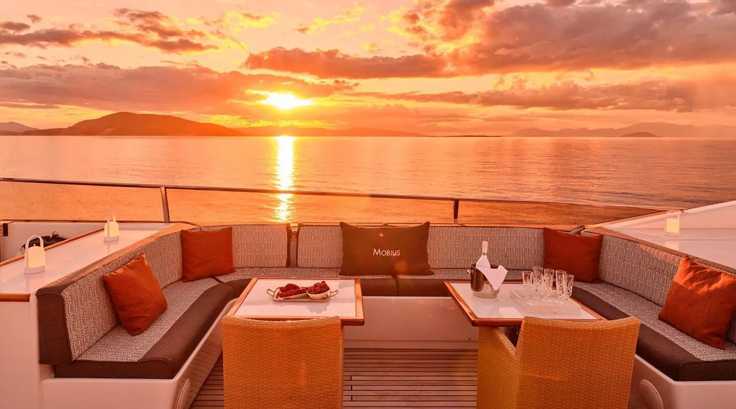 Mobius yacht on calm sea at sunset, outdoor seating, warm orange sky