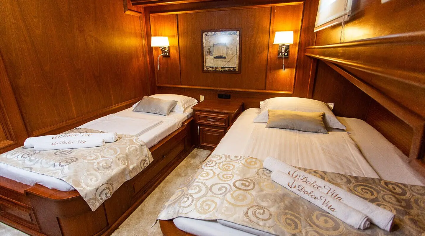 Dolce Vita yacht interior with two single beds, wood panels, and porthole windows