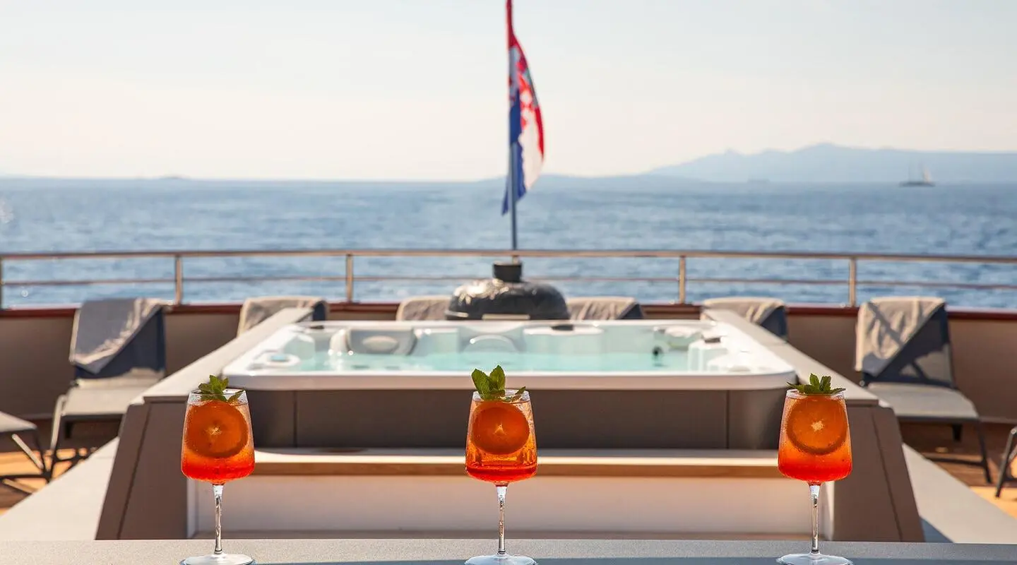 Yolo yacht on sun deck with seating and railings; sea and distant shore in background