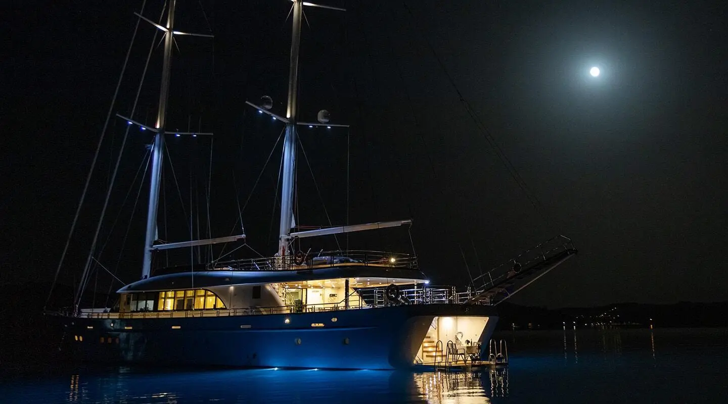 Night view of Love Story yacht at anchor with blue hull and lit deck