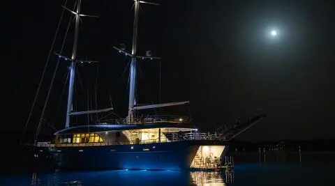 Night view of Love Story yacht at anchor with blue hull and lit deck
