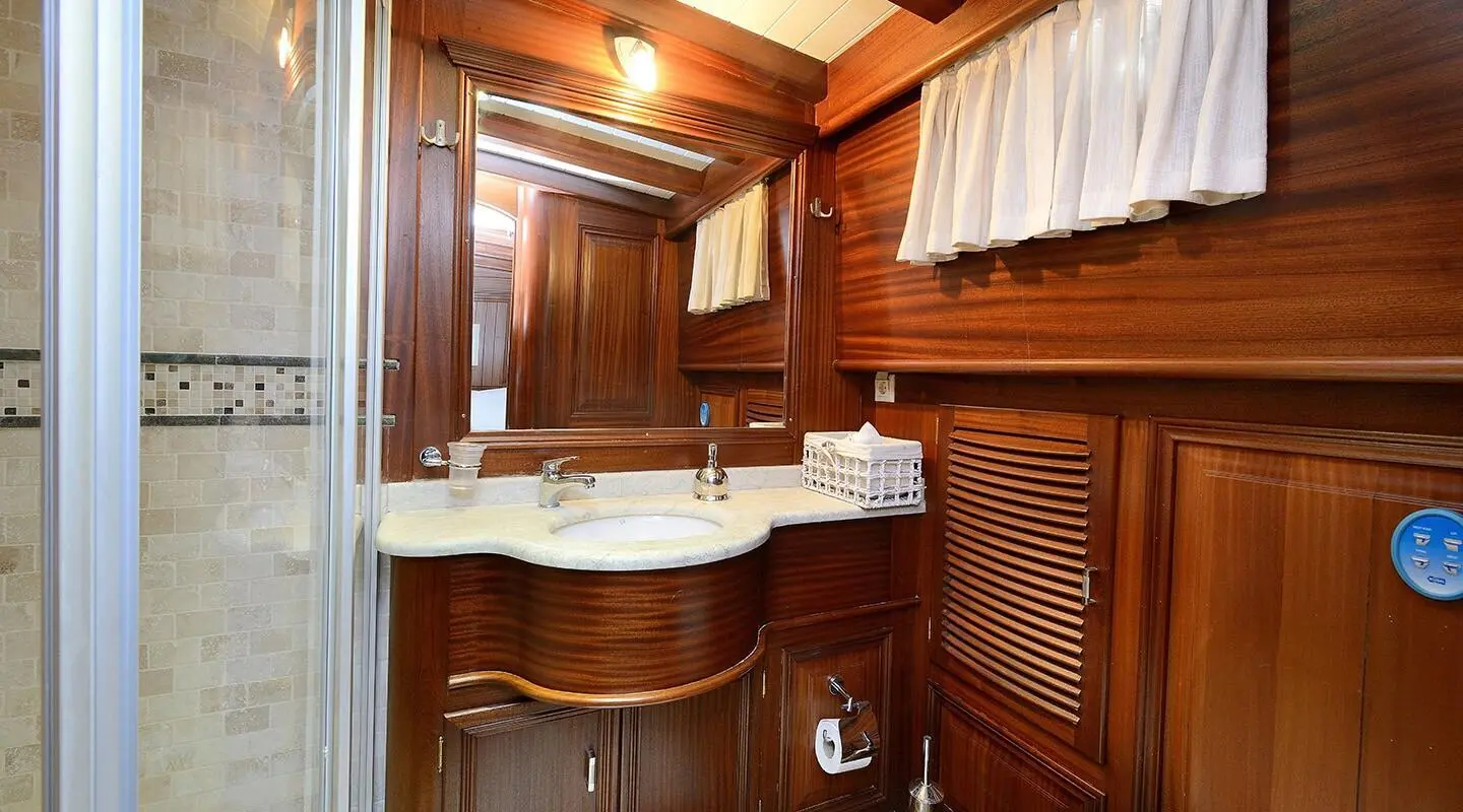 View of a luxury yacht interior with wooden cabinets, curved white sink, and brass fixtures at sunset