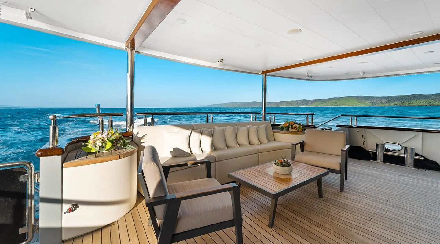 Freedom yacht aft deck with cream lounge seating and teak table overlooking blue ocean
