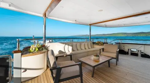 Freedom yacht aft deck with cream lounge seating and teak table overlooking blue ocean