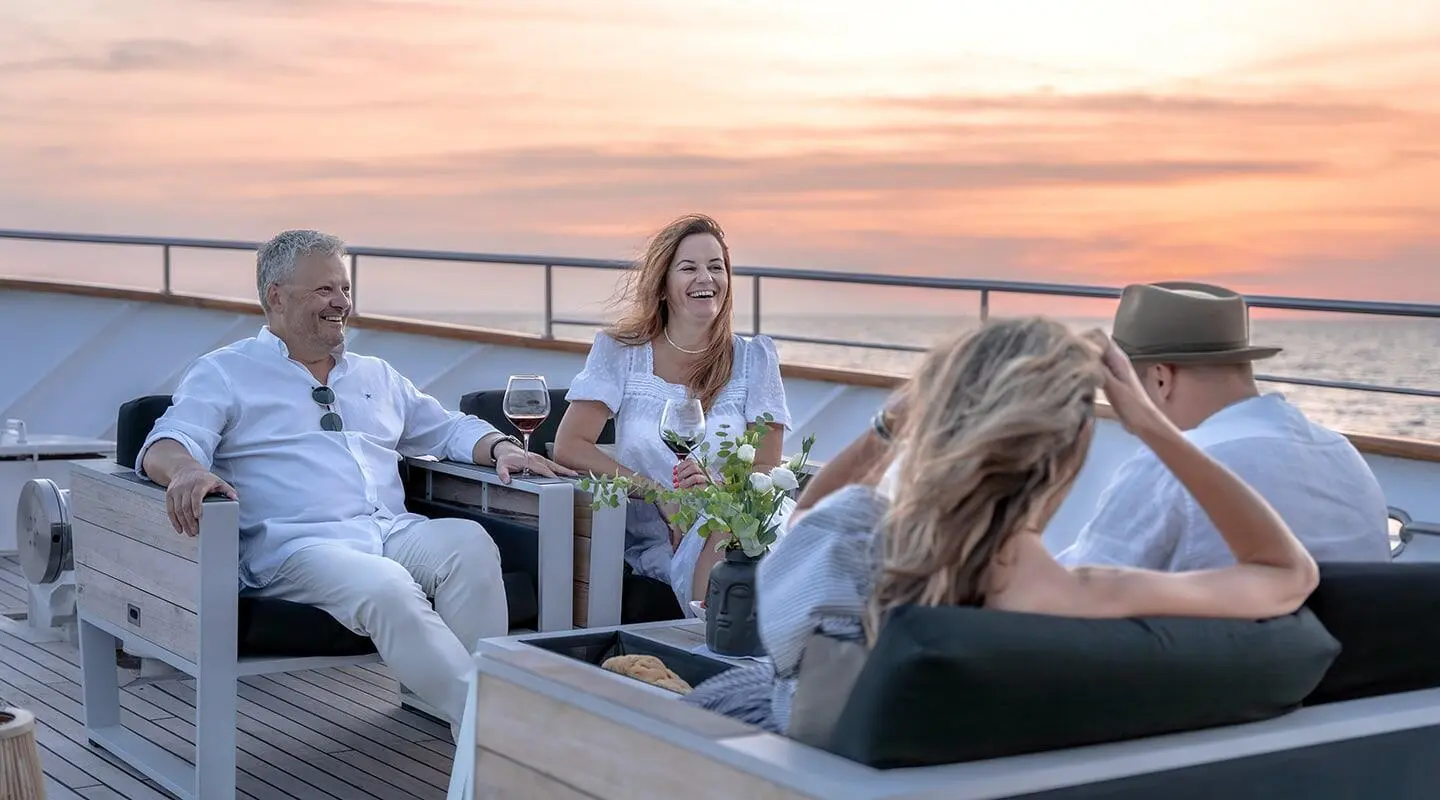 Karizma yacht charter on deck at sunset with guests lounging and conversing