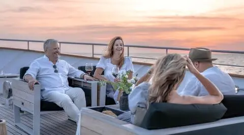 Karizma yacht charter on deck at sunset with guests lounging and conversing