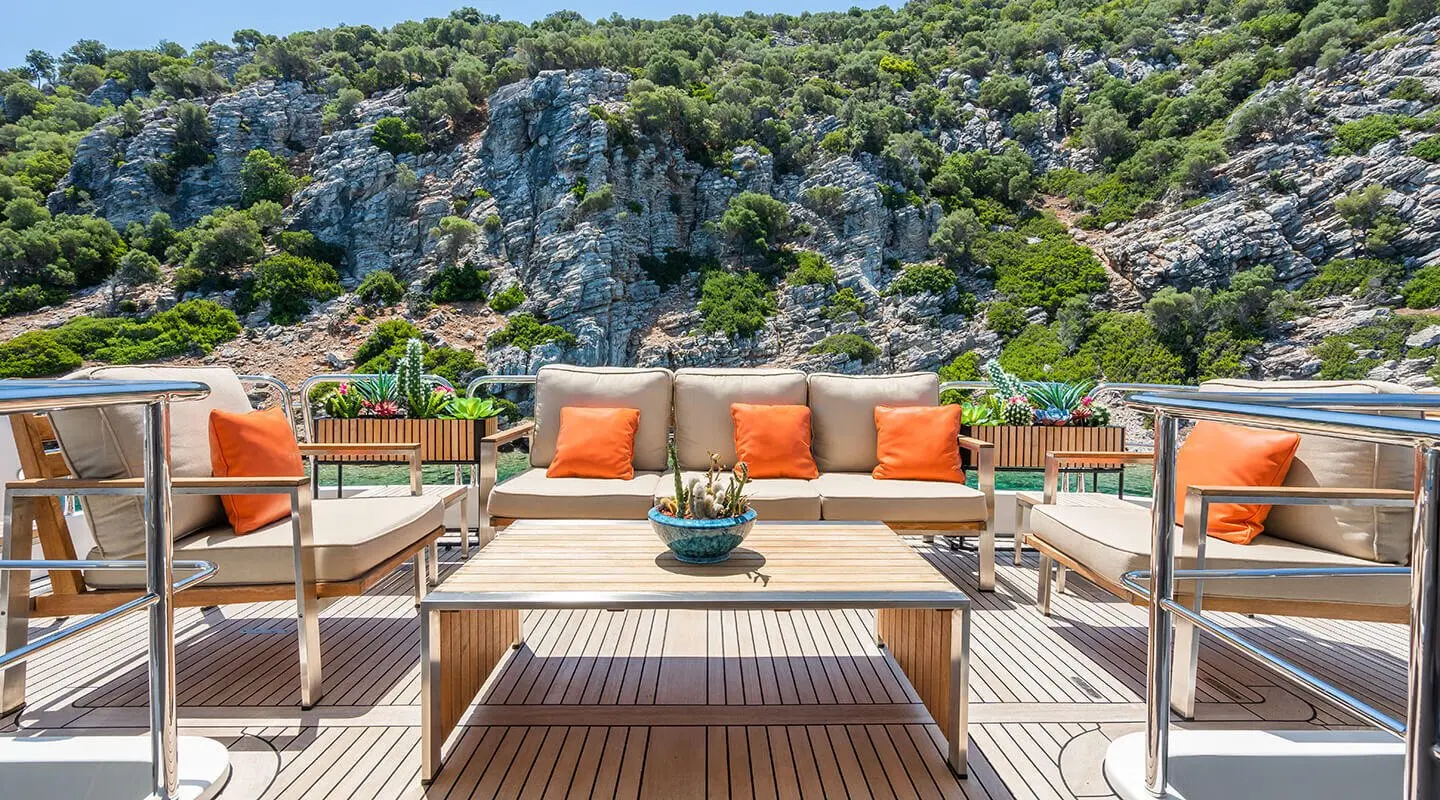 Amadea yacht deck with wooden seating area and orange cushions under clear sky