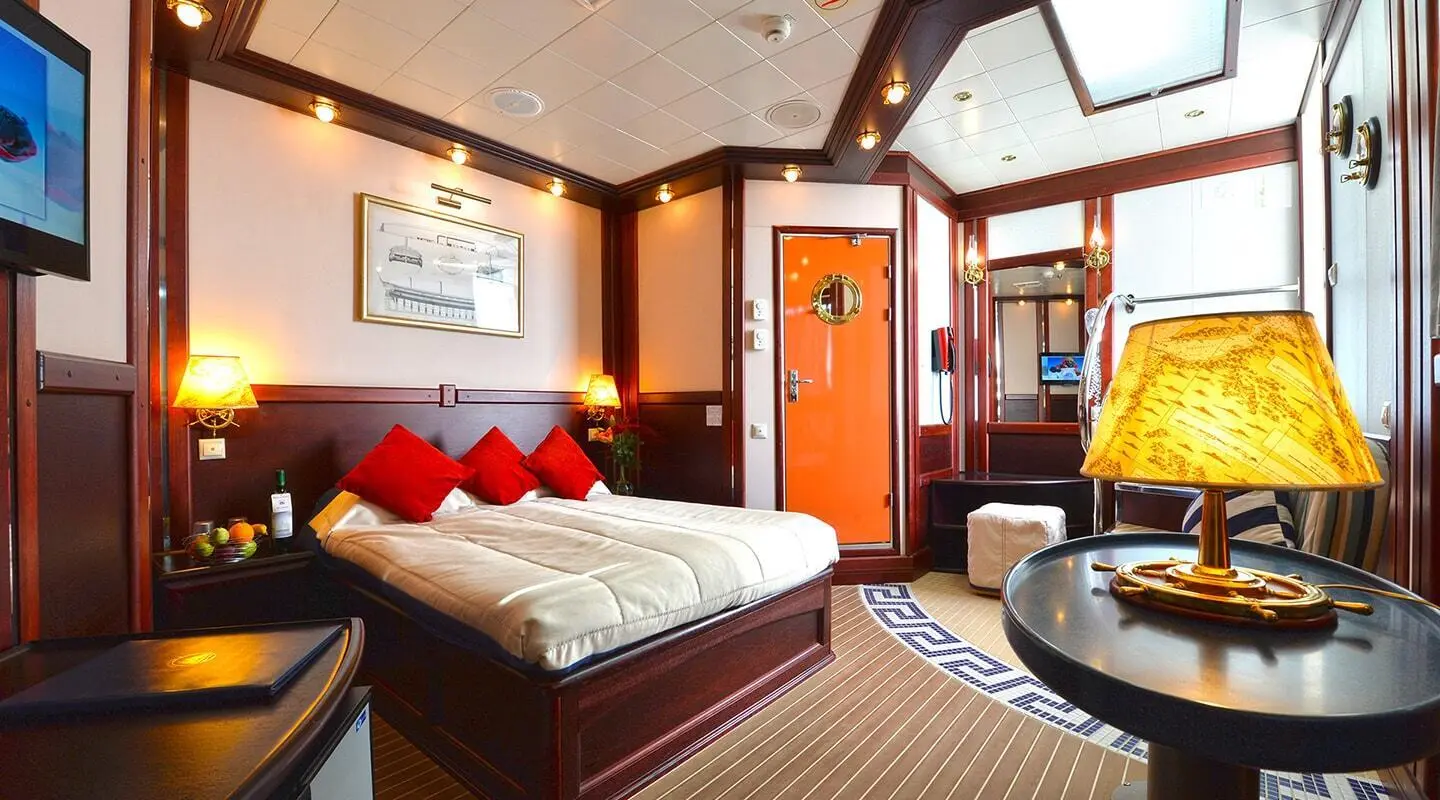 Luxurious yacht interior with a large bed, red throw pillows, and wood-paneled walls
