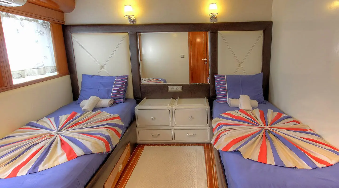 Interior of Angelo II yacht with twin beds, striped bedding and wooden cabinets