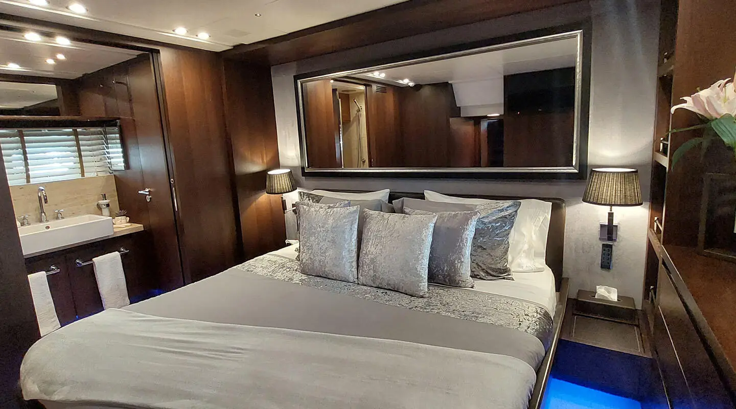 Miraval yacht bedroom with large bed, white linens, and wooden cabinetry