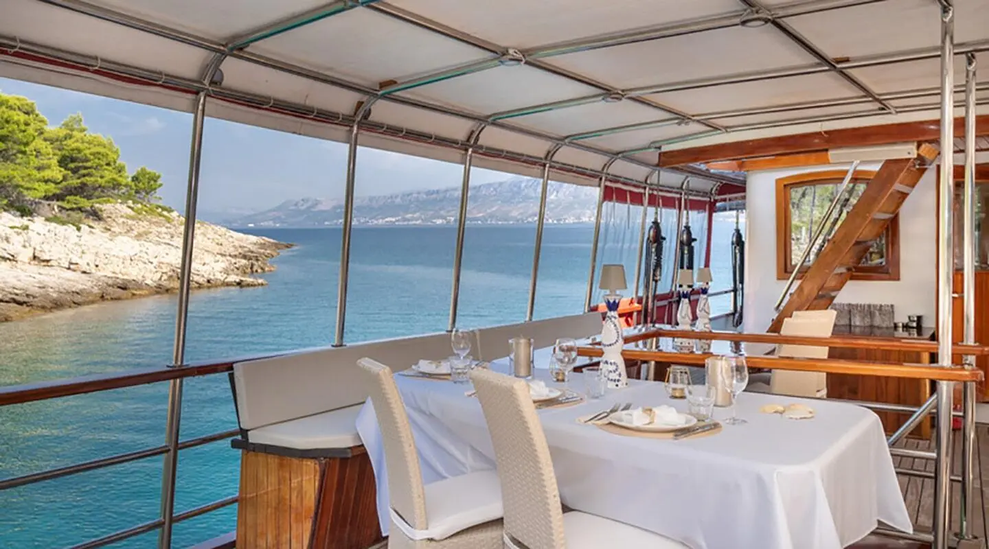 Barbara yacht balcony dining on a covered deck with sea view and rocky coastline