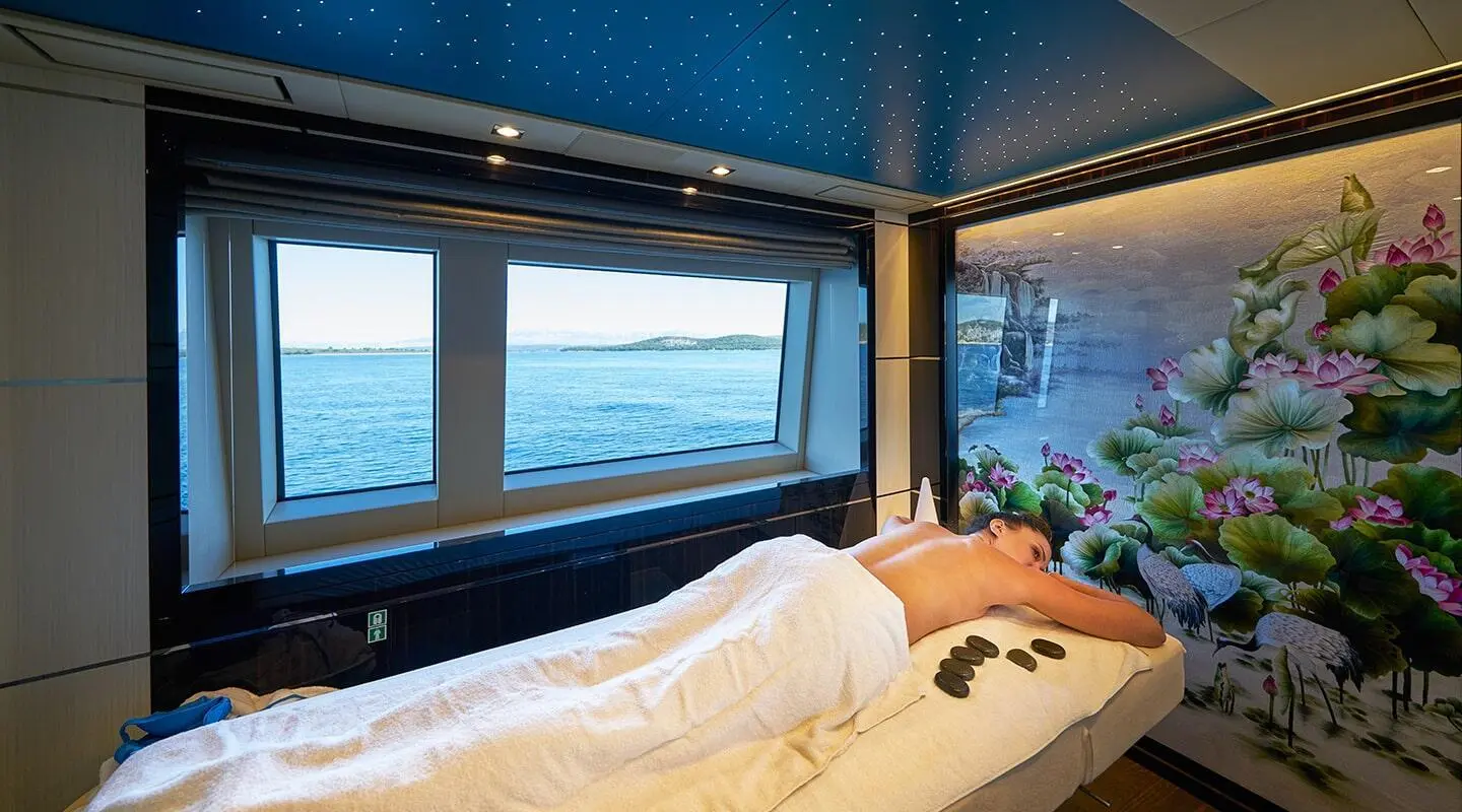 Interior cabin on a yacht named Happy Me with bed facing large window to sea sunset