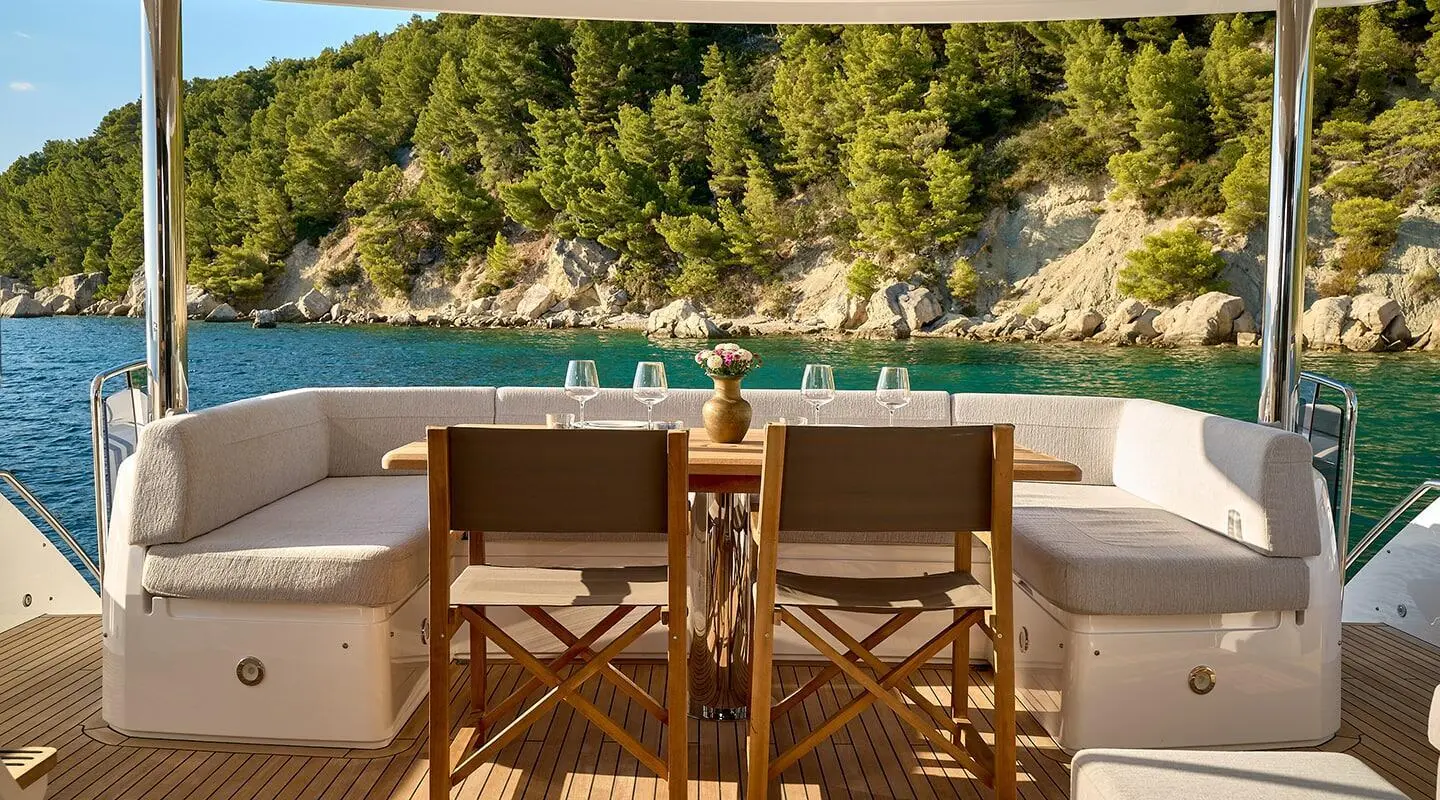 Deck dining area on Hideaway yacht with wooden chairs and sunlit pool backdrop