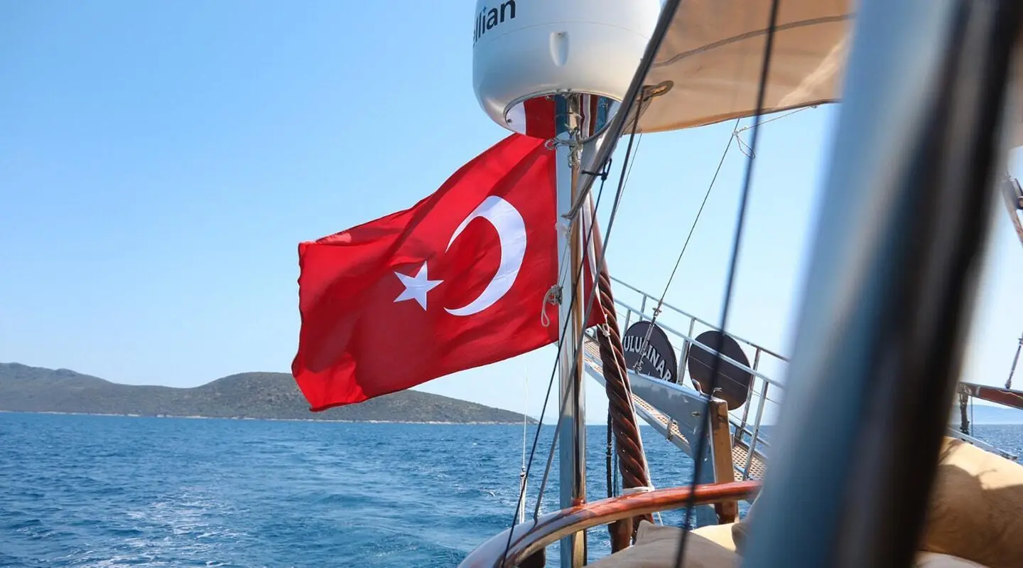 Red Turkish flag on a sailing gulet with blue sea and hills in the background