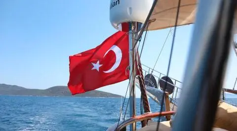 Red Turkish flag on a sailing gulet with blue sea and hills in the background