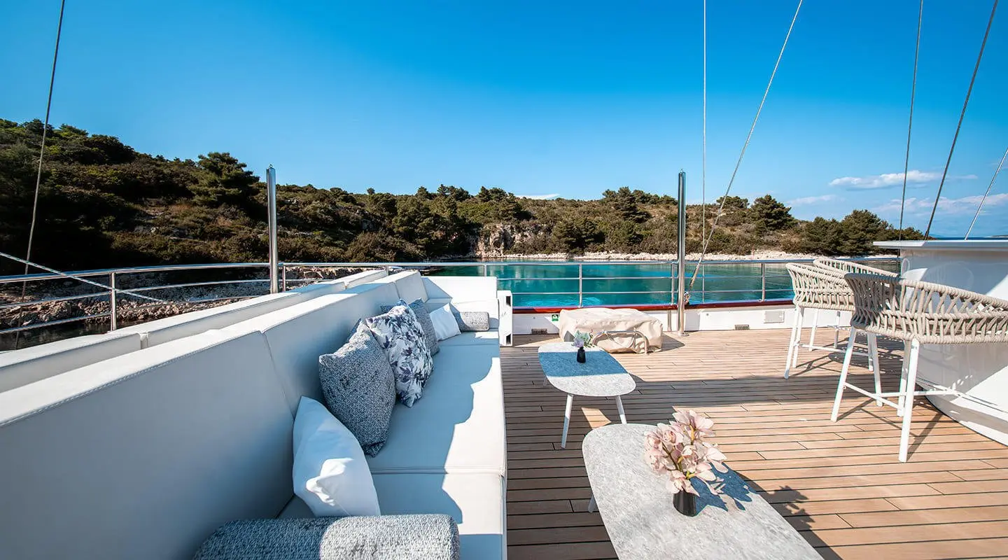 A luxury yacht sundeck with light blue cushions and sun loungers by a pool