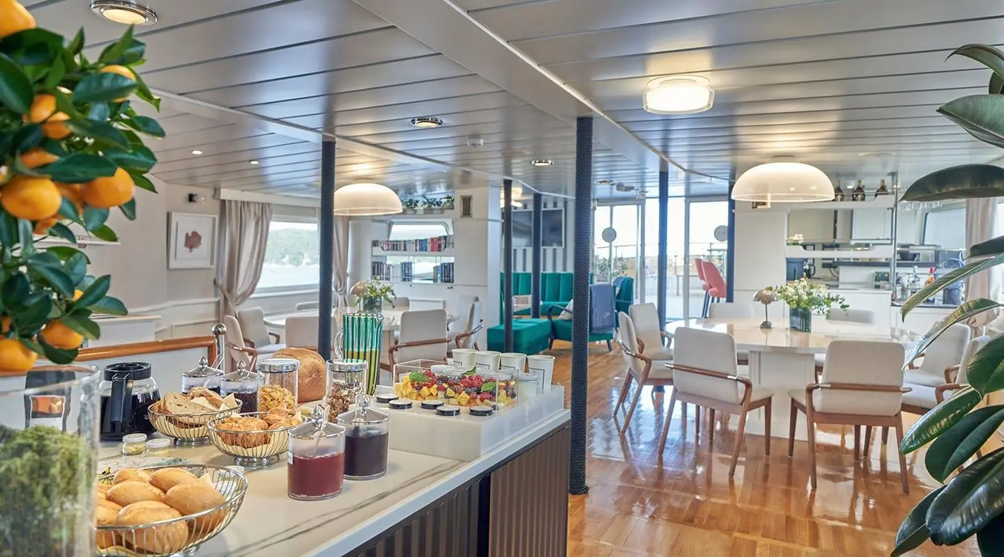 La Perla yacht interior with lounge seating, dining area, and sunlit galley