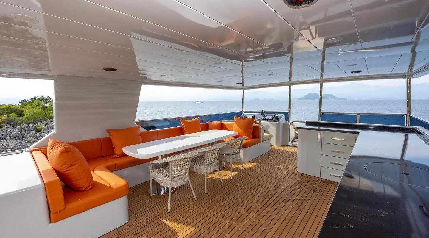 Simay M yacht sun deck with orange seating, table, and large windows at sunset