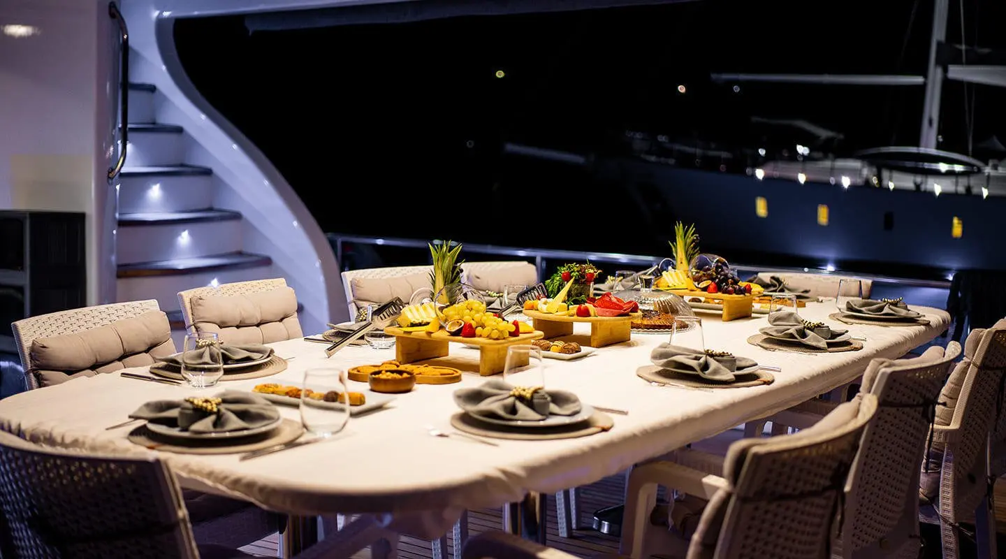 Queen Of Makri yacht at dusk with a long dining table set for guests on deck