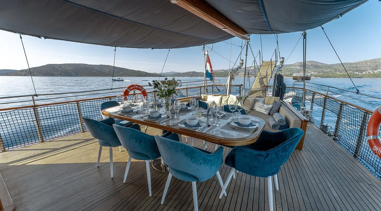 Sunset yacht charter table set with blue chairs and nautical plates aboard a sailing vessel