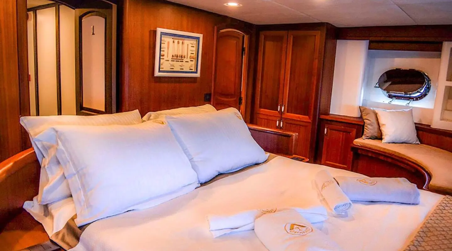 A luxury yacht interior with a large bed, white bedding, and wooden cabinetry