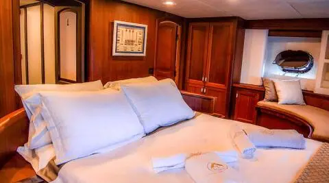 A luxury yacht interior with a large bed, white bedding, and wooden cabinetry