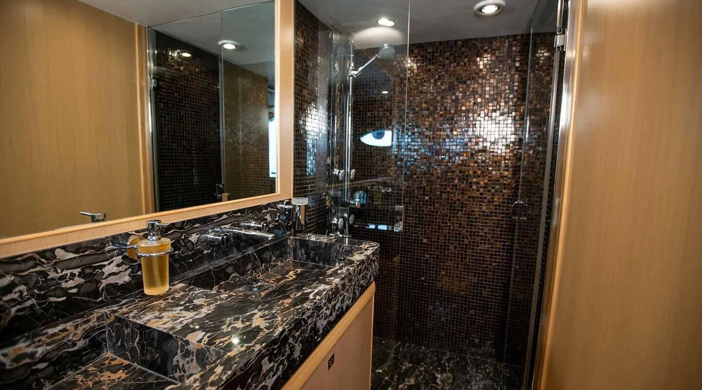 Luxurious yacht bathroom with dark marble sink counter and glass shower enclosure