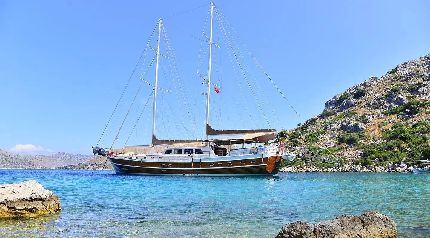 Prenses Bugce yacht anchored near rocky coastline at sunset with clear blue water