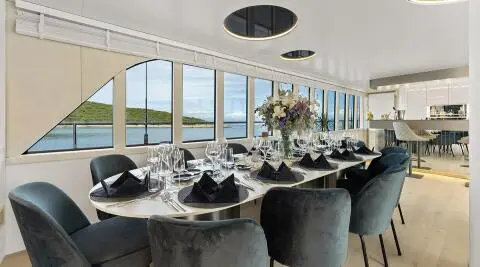 Interior dining area aboard Maxita yacht with long table set for guests, large windows, and elegant seating