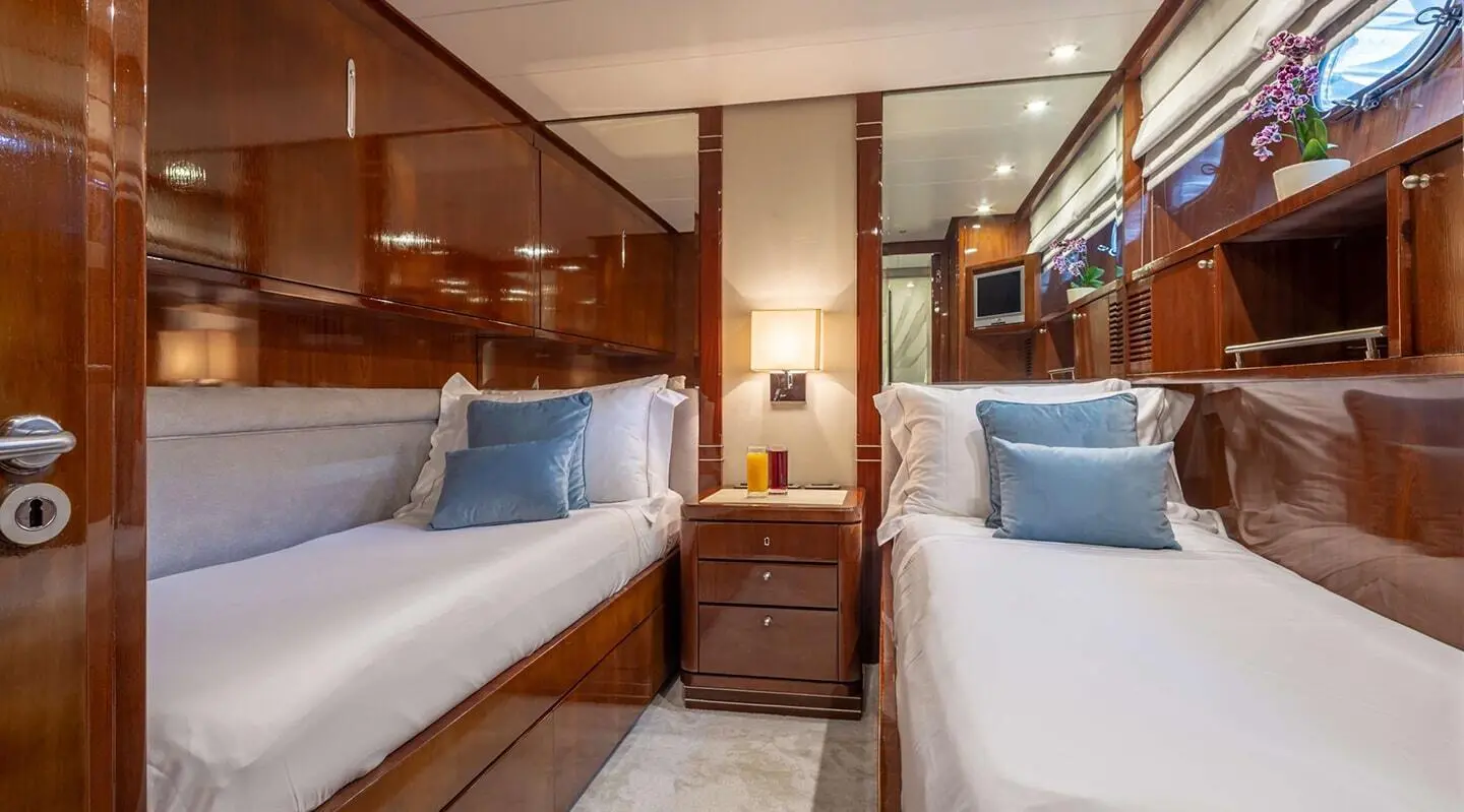 Two side-by-side yacht cabins with neatly made beds and blue pillows