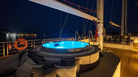 Love Story yacht with blue circular hot tub on deck at dusk