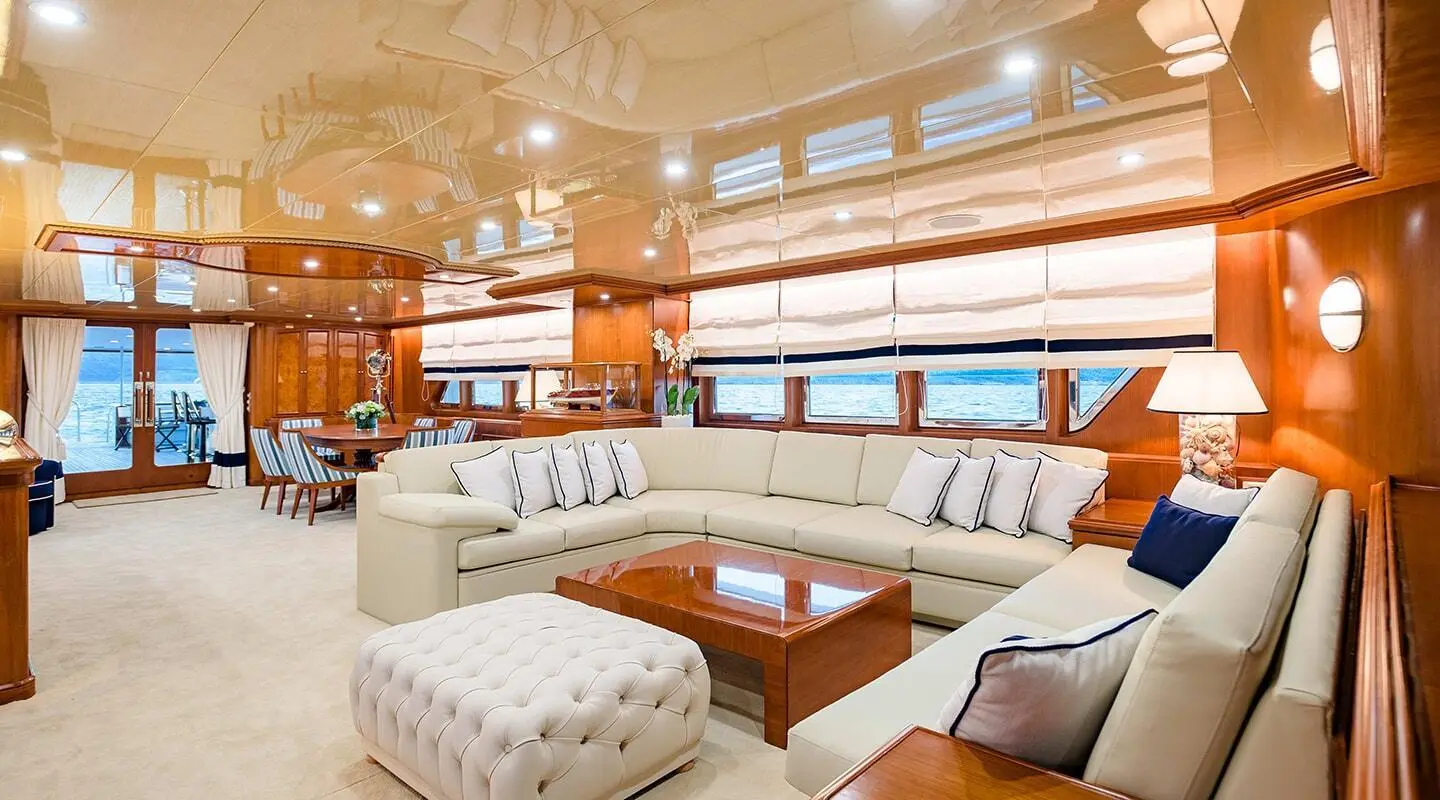 Luxurious yacht saloon with cream seating, wooden tables, and large windows