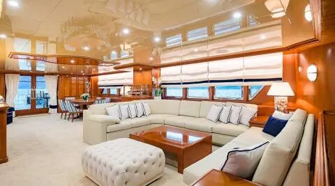 Luxurious yacht saloon with cream seating, wooden tables, and large windows