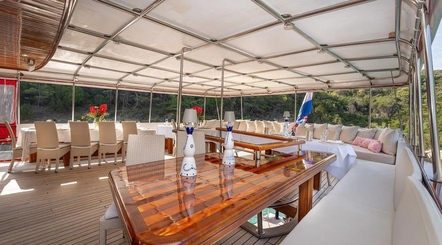 Sunlit yacht Barbara deck with polished wooden table and white seating