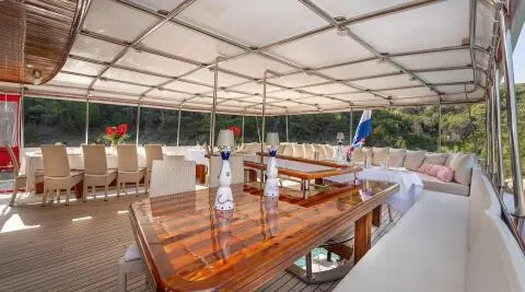 Sunlit yacht Barbara deck with polished wooden table and white seating