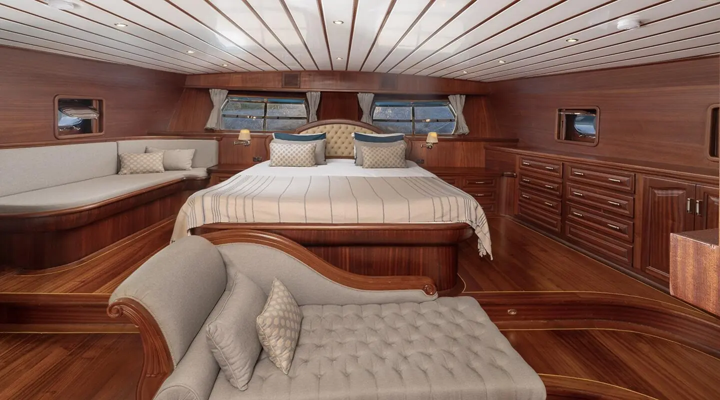Inside cabin with wooden panels, large bed, upholstered seating, and windows