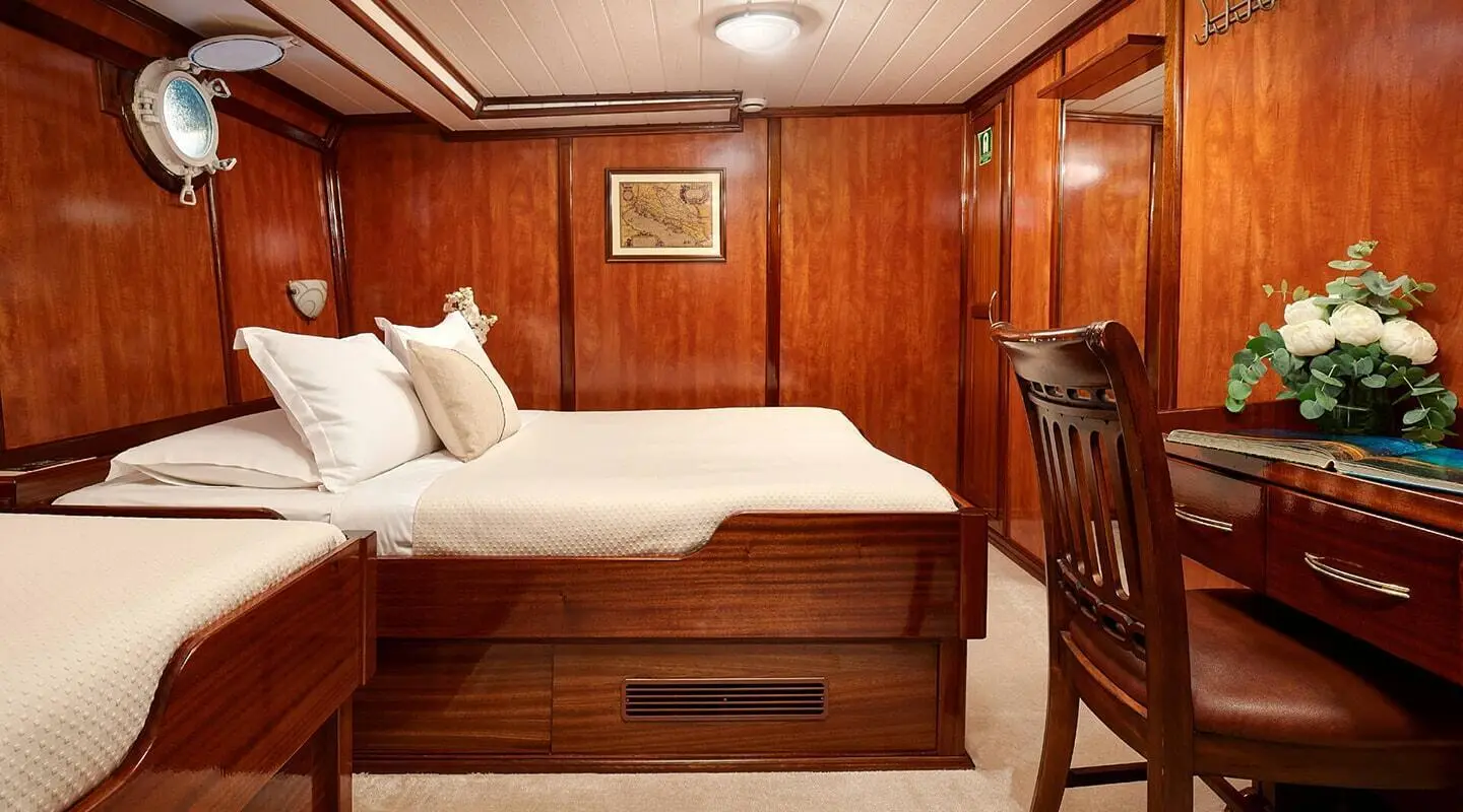 Wood-paneled cabin with a bed, desk, and flowers on a yacht interior