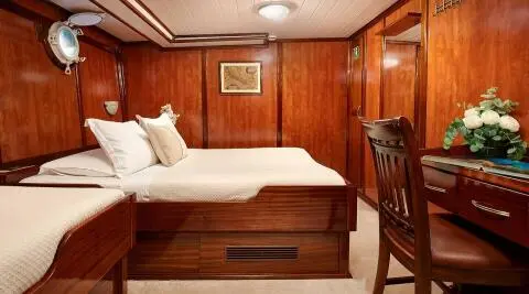 Wood-paneled cabin with a bed, desk, and flowers on a yacht interior