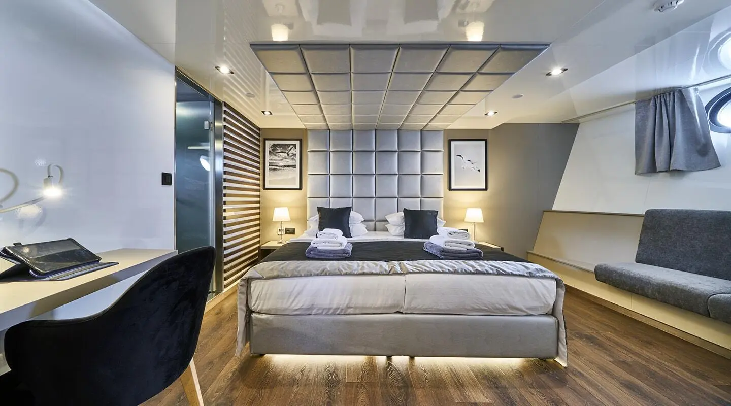 Luxurious cabin on Rara Avis yacht with bed, pillows, and warm lighting