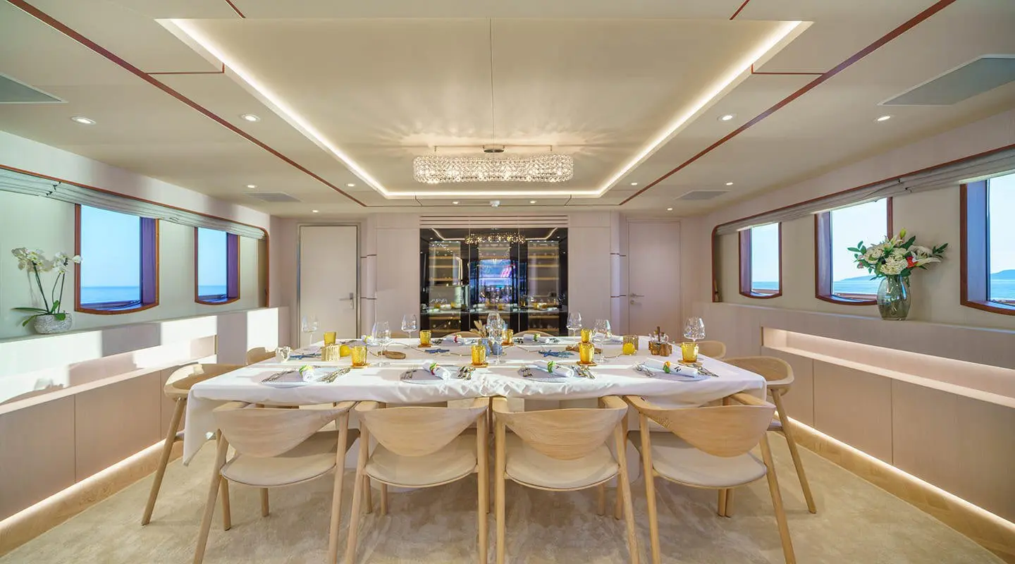 Maia yacht dining saloon with long table, chairs, and warm ambience