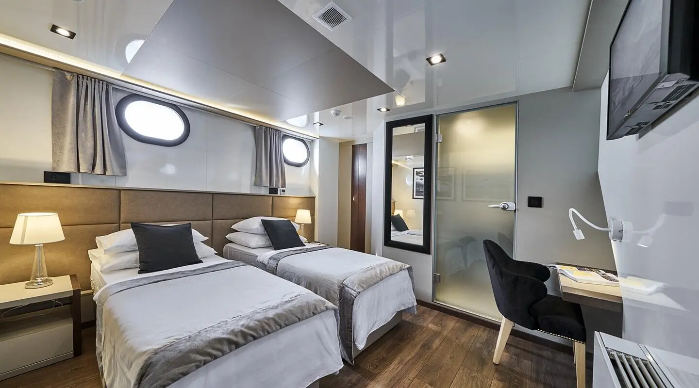 Twin cabin aboard Rara Avis gulet with two beds, porthole, and wood accents
