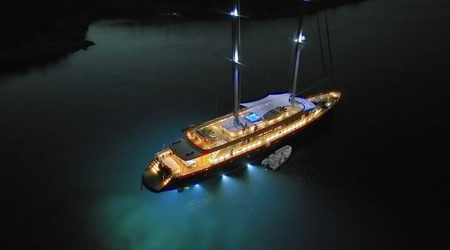 Dalmatino yacht at sea at dusk, warm lights glow from deck